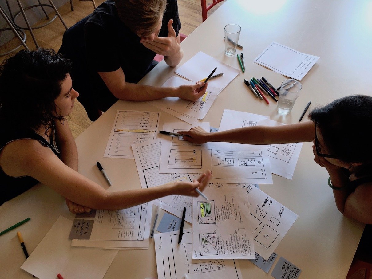 Three designers discussing concept sketches around a table