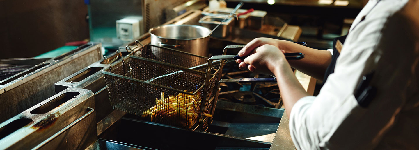 A hospitality employee pulling french fries out of the fryer.
