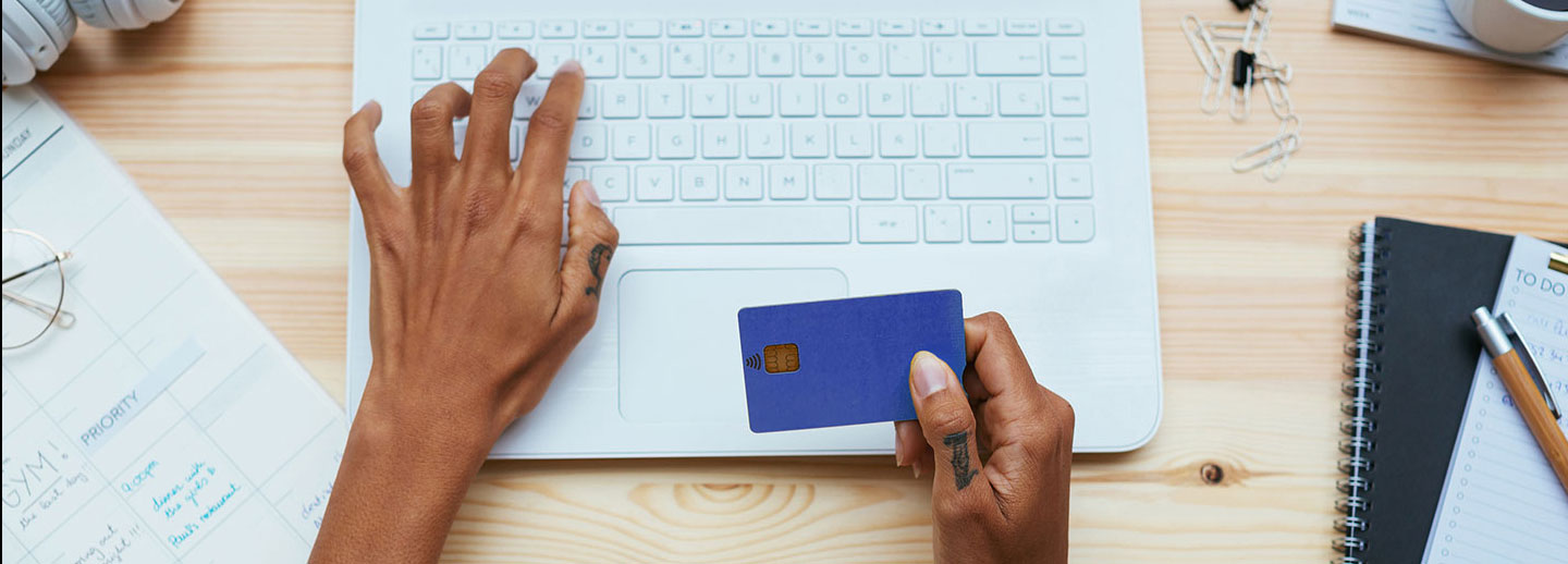 A woman holding her credit card with her right hand while typing into her laptop with the other.