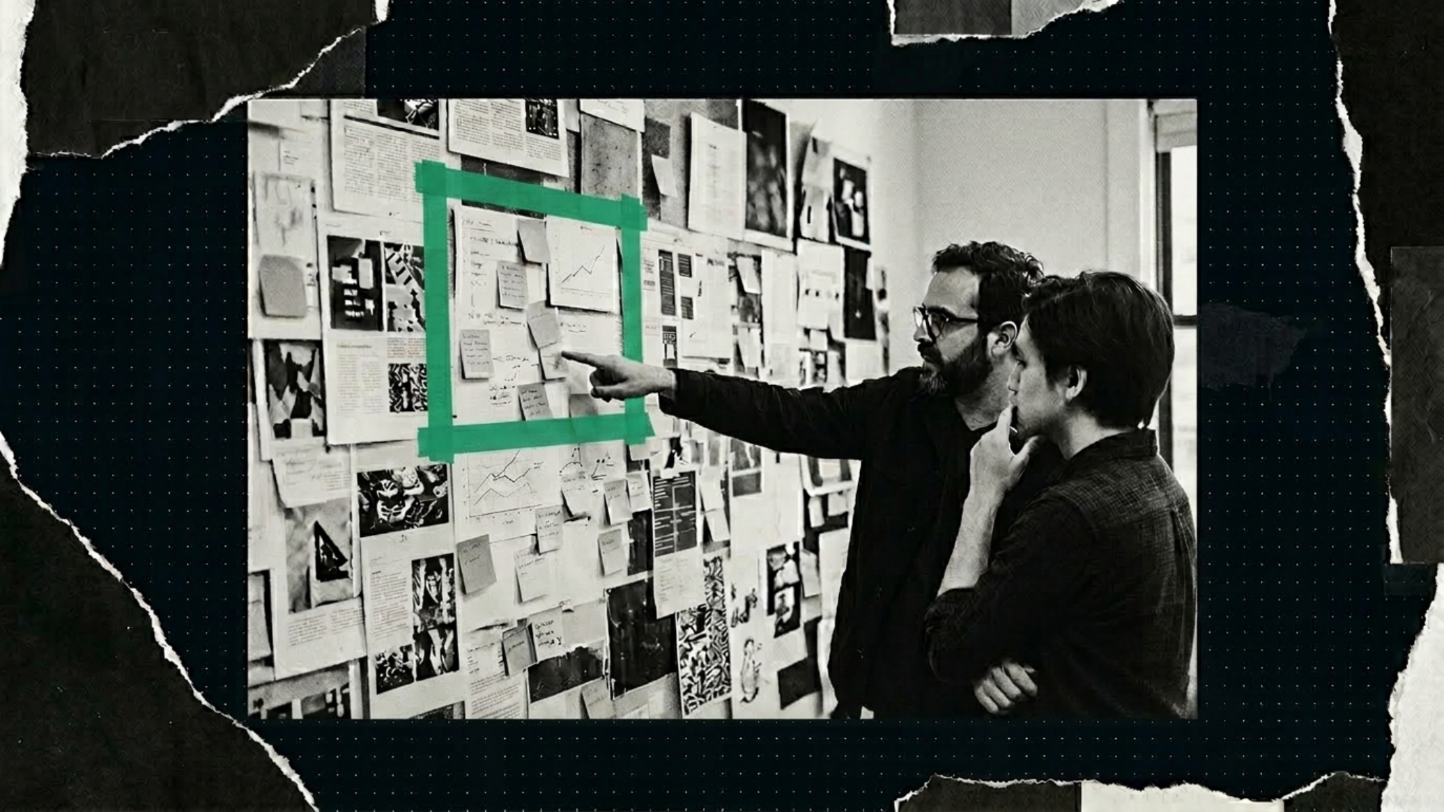 Two designers reviewing a research wall covered in sticky notes and printed layouts, one pointing into a section framed by green tape — the defined constraint zone both figures are focused on.