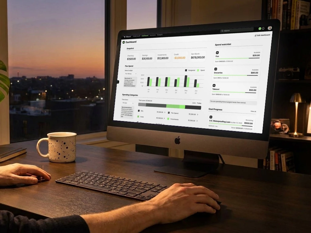 Hands on a keyboard and mouse at a desktop computer in an evening home office, showing the Beacon AI personal finance dashboard